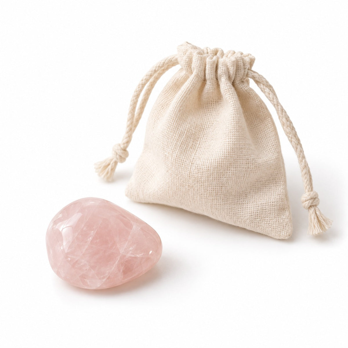 Tumbled rose quartz stone next to a cotton pouch on a white background