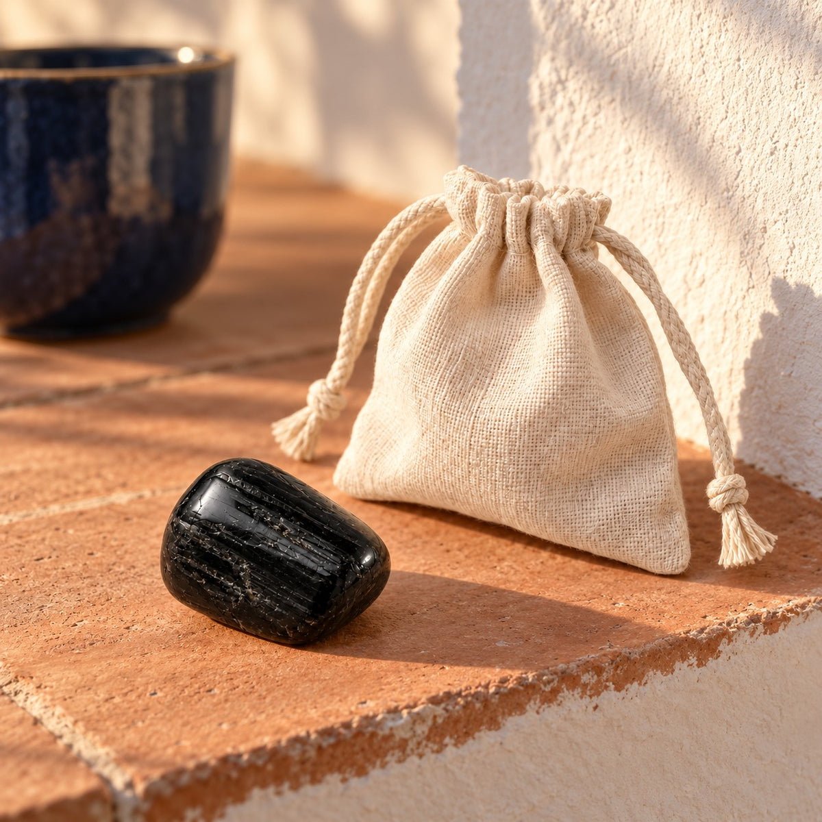 Tumbled black tourmaline stone on a terracotta ledge in warm sunlight