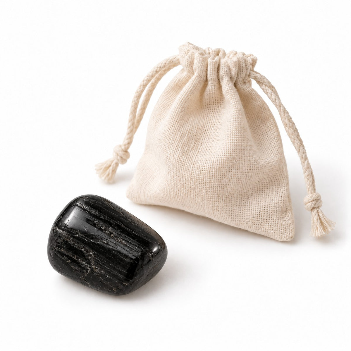 Tumbled black tourmaline stone next to a cotton pouch on a white background