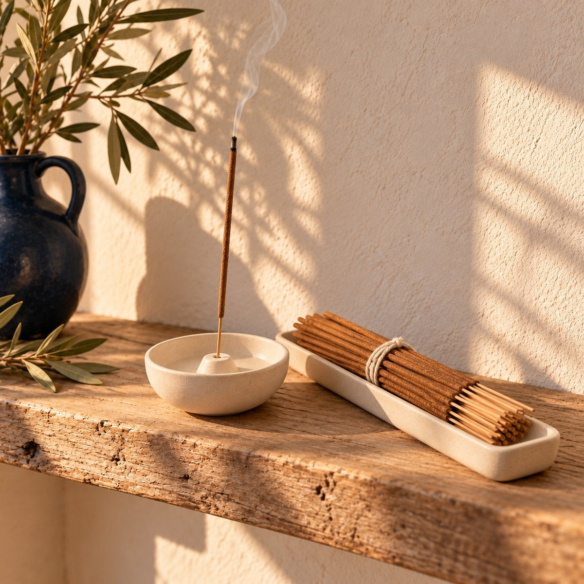 Palo santo incense set on a wooden shelf, one stick burning in the ceramic bowl